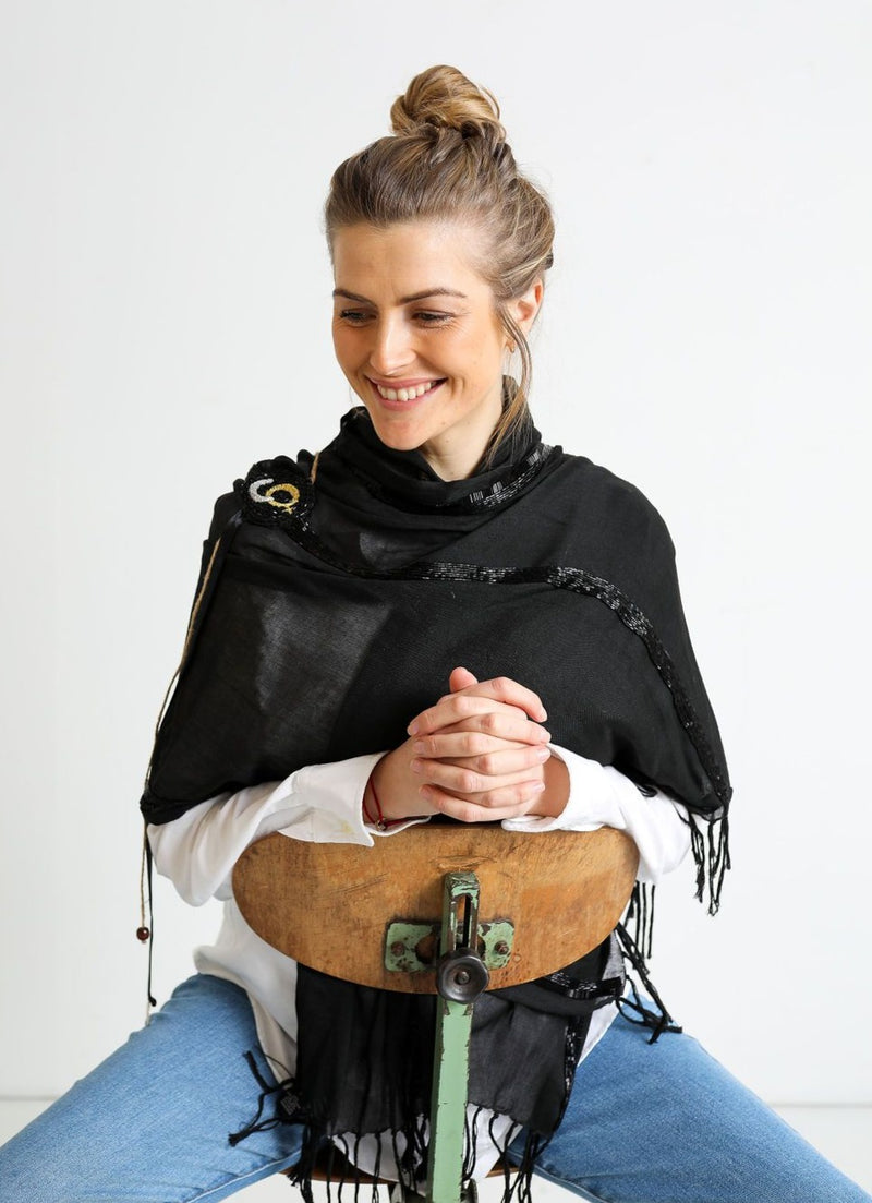 De duurzame, handgemaakte, betekenisvolle Stripe sjaal in zwart die elegant gedrapeerd is en een intrigerend patroon van verweven kleuren en texturen laat zien
