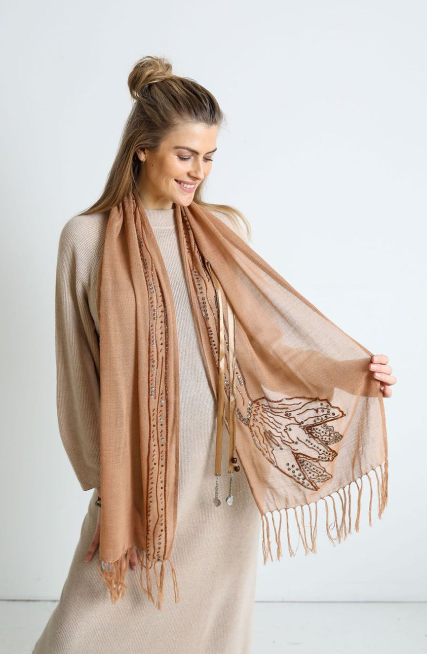 De duurzame, handgemaakte, betekenisvolle Tulip sjaal in beige die elegant gedrapeerd is en een intrigerend patroon van verweven kleuren en texturen laat zien